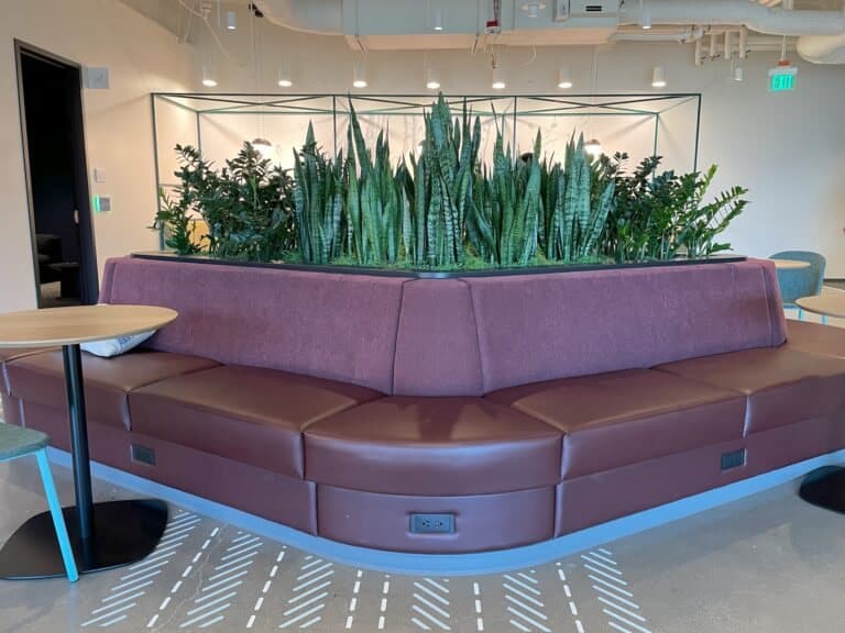 Round upholstered waiting room seating built around a central planter of lush greenery.