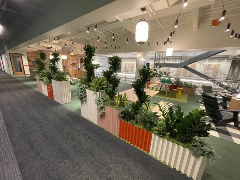 Modern workplace lounge with comfortable seating surrounded by lush green planting.