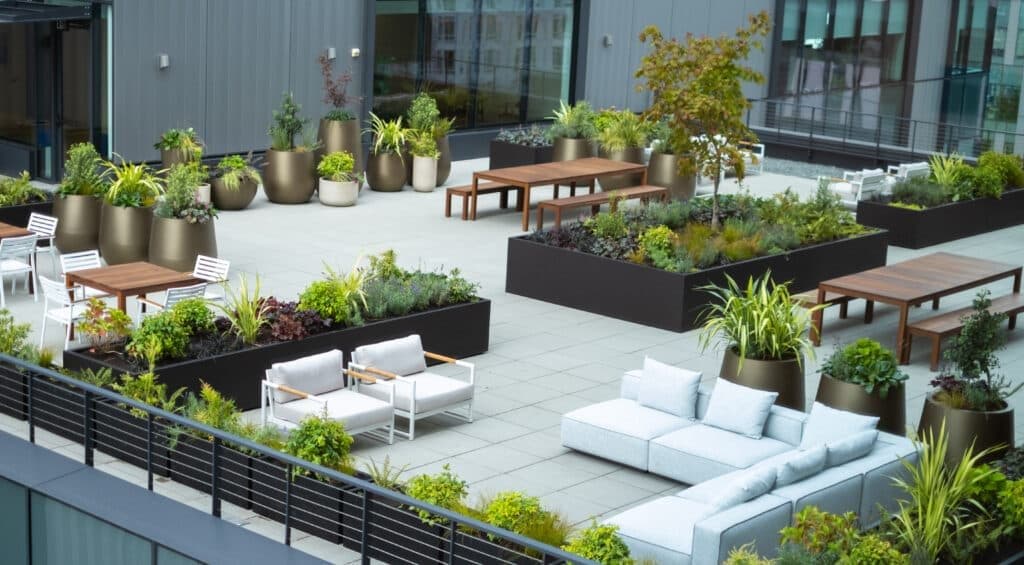 Rooftop terrace with charcoal and bronze planters, outdoor lounge seating and a timber dining table surrounded by mixed greenery.